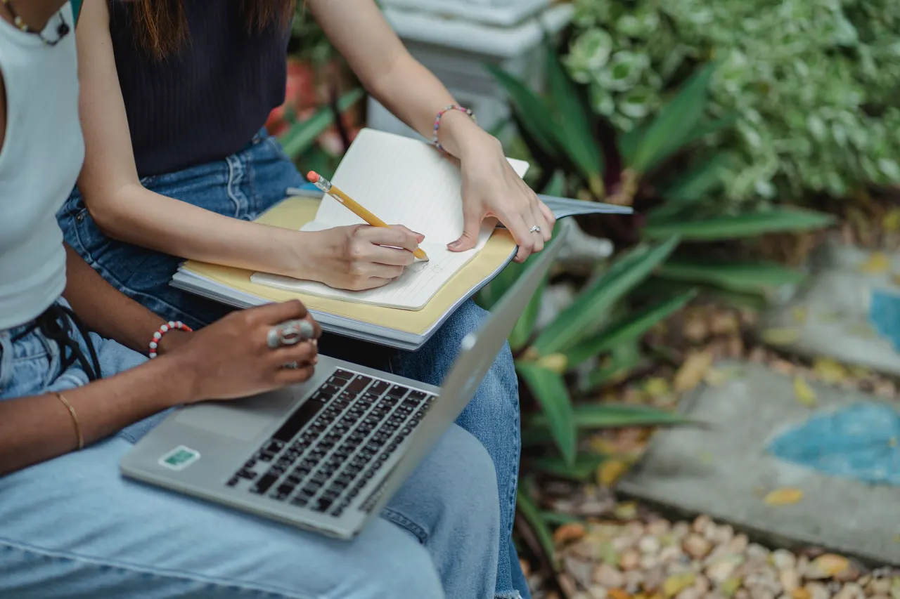 Crop unrecognizable diverse female students working on project in park